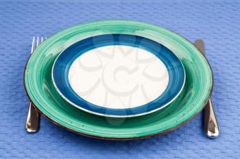 Two colorful empty plates with knife and fork on blue cotton towel.