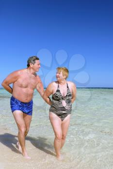 Mature couple walking on the beach in tropical resort.