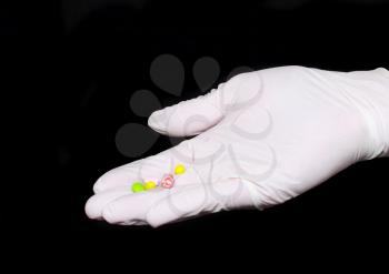 Hand holding a capsule or pill in medical gloves, on black background.