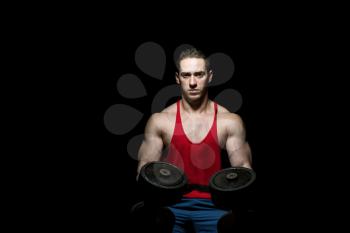 young bodybuilder posing with dumbbell at the bench on black background