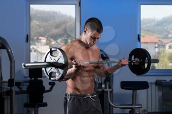Young Athlete Doing Heavy Weight Exercise For Biceps With Barbell - On A Blue Background