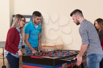 Group Of Young Men And Women Enjoying A Game Of Foosball