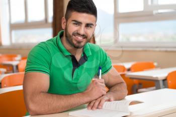 Portrait Of Young Arabic Male College Student With Book Sitting In Classroom Alone