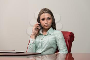 Beautiful Young Business Woman Sitting At Office Desk And Talking On Cell Phone - City Businesswoman Working