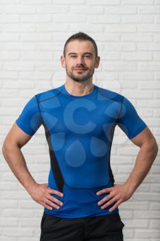 Personal Trainer Standing Strong On White Bricks Background With Copyspace And Flexing Muscles - Muscular Athletic Man Fitness Model Posing