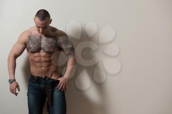 Portrait of a Strong Man In Pants Showing His Abs Standing Isolated on Gray Background