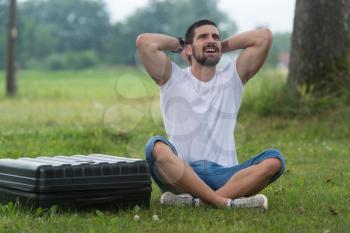 Portrait of Frustrated Young Engineer Sitting On Grass With Case from Drone