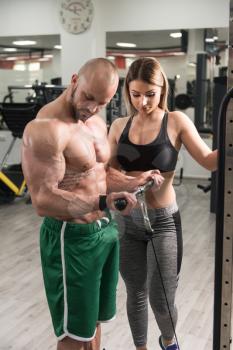 Personal Trainer Showing Young Woman How To Train Biceps In The Gym