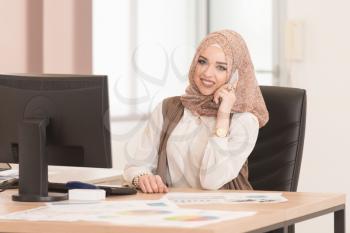 Young Cheerful Muslim Business Woman Working With Computer At Desk In The Modern Office And Talking On Phone