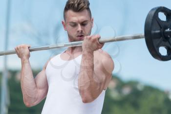 Man Working Out Biceps In Outdoors With Barbell