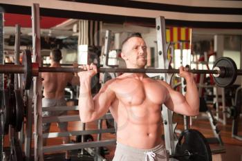 Muscular Man Doing Heavy Weight Exercise For Shoulders With Barbell In Gym