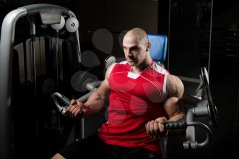 Muscular Fitness Bodybuilder Doing Heavy Weight Exercise For Biceps On Machine With Cable In The Gym