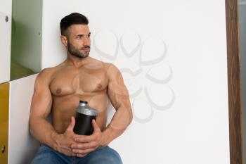 Young Man Resting In Gym Dressing Room With Supplements Shaker for Copy Space - a Place for Your Text