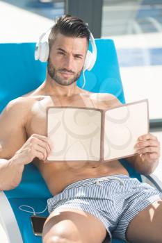 Young Man Resting On Sun Loungers By Swimming Pool and Listening Music On Headphones