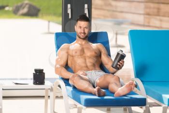 Young Man Resting On Sun Loungers By Swimming Pool With Supplements Pills And Dope or Shaker for Copy Space - a Place for Your Text