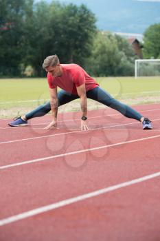 Sporty Man Stretching and Warming Up Legs for Running Fitness Workout on Track Exercising Outside