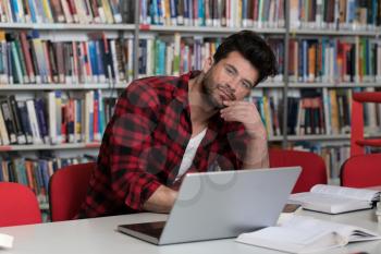 Male College Student Looks Tired While Studying With a Laptop and Textbooks in the Library