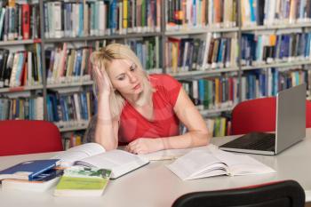 Female College Student Looks Tired While Studying With a Laptop and Textbooks in the Library