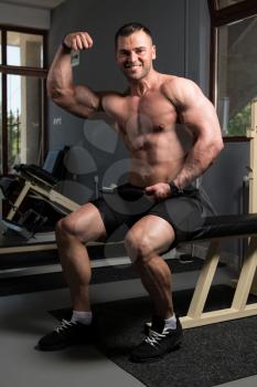 Handsome Young Man Sitting Strong In The Gym And Flexing Muscles - Muscular Athletic Bodybuilder Fitness Model Posing After Exercises
