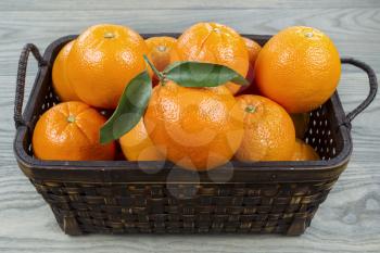 Horizontal photo of basket full of ripe oranges on faded wooden table