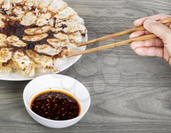 Hand holding chopsticks with Chinese dumplings on white plate with wood table in background