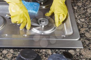 Hands wearing gloves cleaning gas burner with cover removed