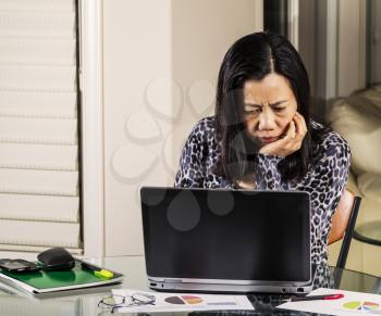 Mature women looking confused at information on computer while working from home