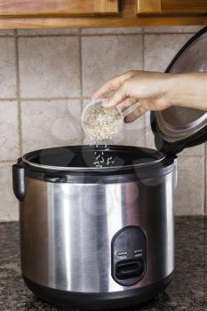 Hand pouring brown and white rice into rice cooker on stone counter top in kitchen