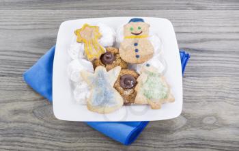 Variety of homemade holiday cookies in white plate on faded wooden table with blue cloth napkin