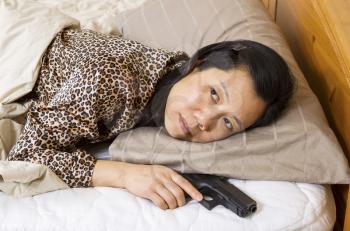 Horizontal photo of mature woman holding personal weapon, pistol, while in bed