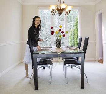 photo of mature woman placing bamboo chopsticks on place mats in family formal dining room with daylight coming through large windows in background