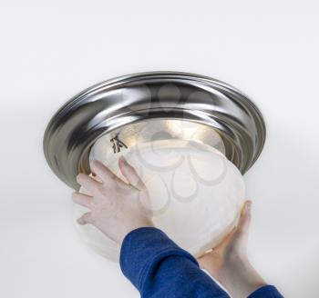 Photo of female hands installing glass lid over new light bulbs with white ceiling in background