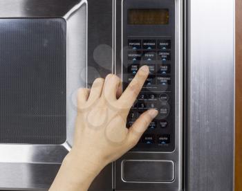Hand preparing to activate defrost mode on microwave oven