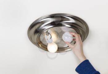Horizontal photo of hand taking out light bulb- incandescent type- with one bulb burnt out and one working
