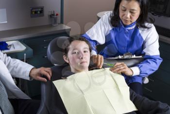 Horizontal photo of a young girl not too excited about being at the dentist off with dentist and woman dental assistant next to her