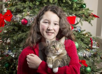 Young girl holding gray hair tabby cat with Christmas tree in background