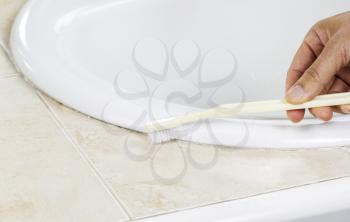 Horizontal photo of female hand with tooth brush cleaning bathroom sink 