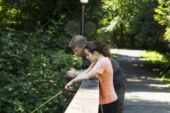 Horizontal photo of young girl and her father fishing off wooden bridge with trees and lamp post in background  