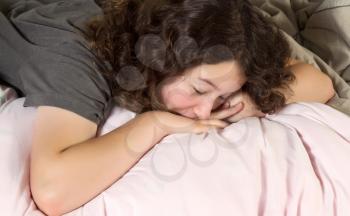 Young girl trying to wake up in the morning with her chin resting on the back of her hands while lying in a messy bed  