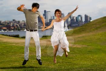 Horizontal photo of young adult couple jumping up together with city of Seattle and Puget Sound Water in Background
