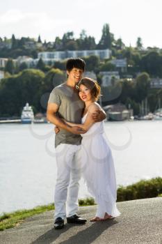 Vertical photo of young adult couple, looking forward, with harbor in Background