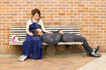Horizontal Photo of young adult woman looking at her lover as he is lying down in her lap with brick wall in background 