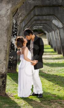 Vertical photo of young adult couple preparing to kiss each other while underneath a structured column wall in background 