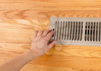 Horizontal photo of female hand opening up heater floor vent with Red Oak Floors in background 