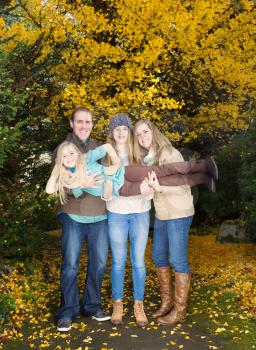 Vertical photo of family holding up their smallest daughter while taking a walk in the park during an autumn day