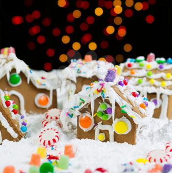 Photo of Gingerbread houses, surrounded by powdered snow, with night lights in background 