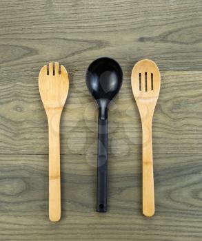 Photo of three kitchen spoons, two of them wooden, on aged white oak boards 