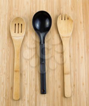 Vertical photo of three kitchen spoons, two of them wooden, on natural bamboo wood 