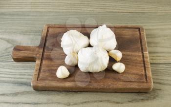 Horizontal photo of fresh raw garlic on black walnut board with aged wood underneath