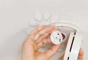 Horizontal photo of female hands examining home smoke detector with white ceiling in background
